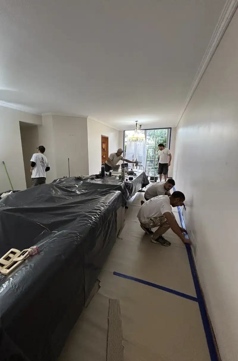 Equipo de pintores encintando zócalos en un living con los muebles cubiertos con nylon y el piso protegido