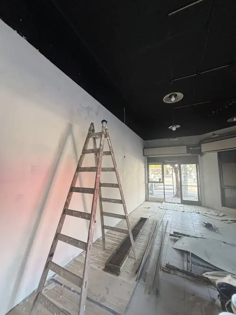 Interior de un local en obra con paredes nuevas enduidas, escalera y cielorraso negro