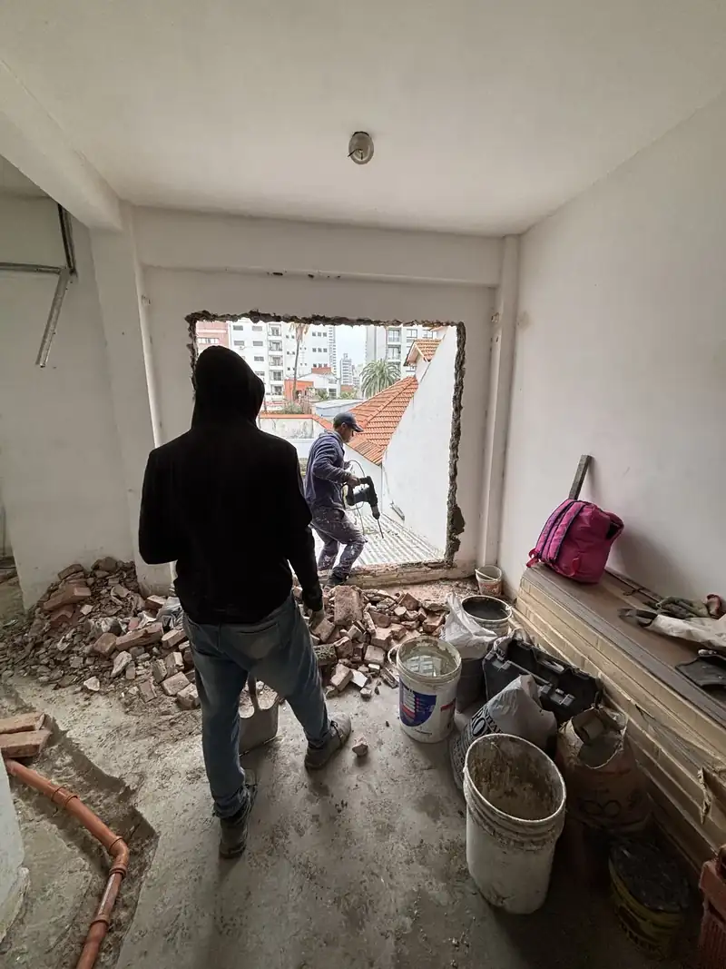 Dos operarios de espaldas demoliendo un muro para abrir un vano en una vivienda