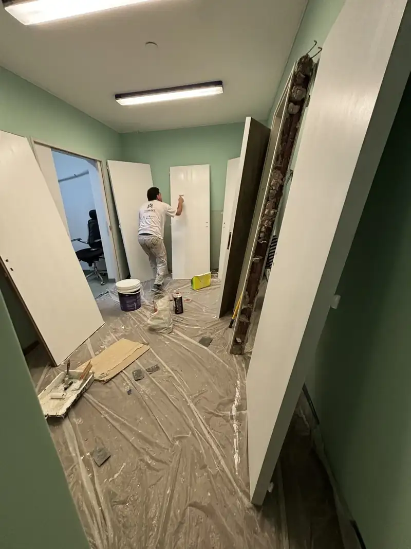Oficina en reforma con el piso protegido y un operario de espaldas pintando un marco