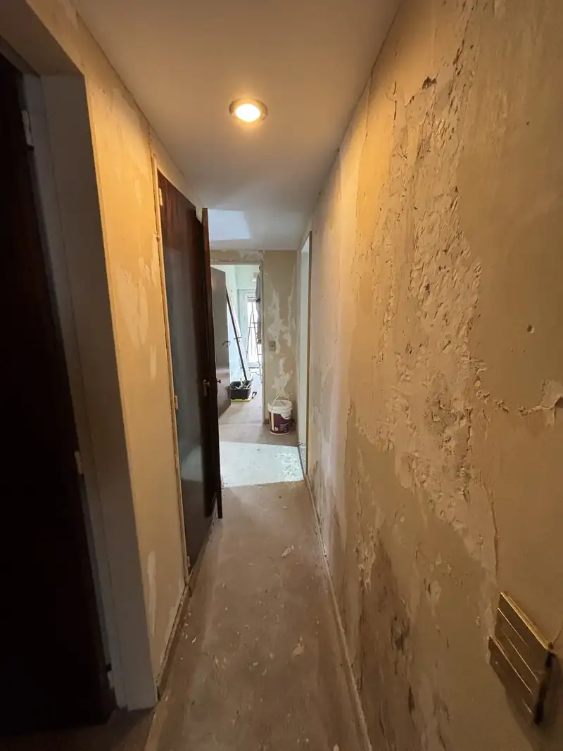 Pasillo con la pintura y el revoque de la pared dañados por la humedad, antes de tratarla