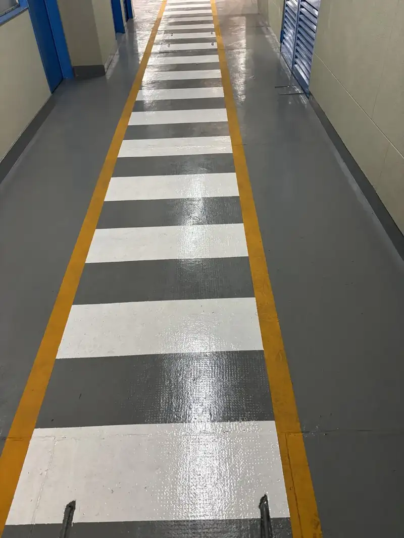 Pasillo industrial con el piso demarcado con franjas blancas y grises y líneas amarillas